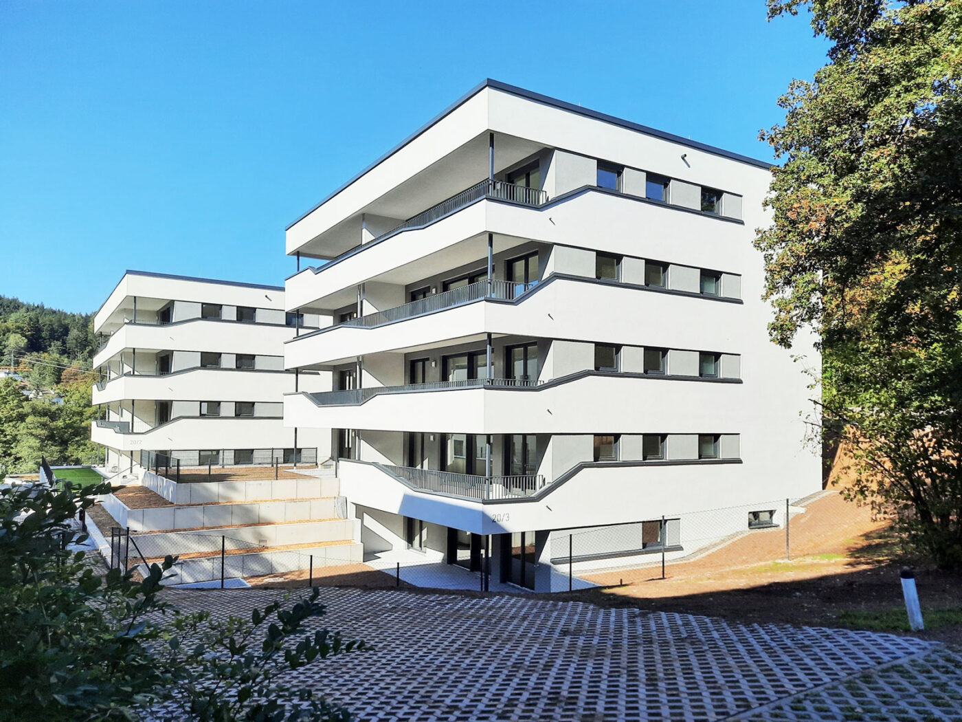 Schiesstal Schwäbisch Gmünd Drei moderne, weiße Neubau-Wohnhäuser mit Balkonen und großen Fenstern unter strahlend blauem Himmel, umgeben von Grünflächen und Bäumen.